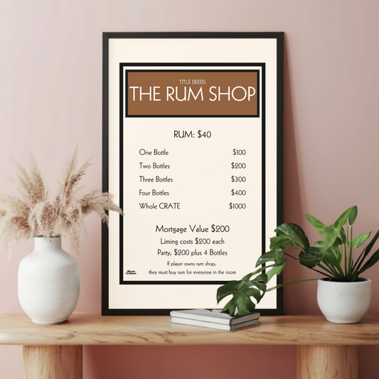 Framed poster titled 'The Rum Shop' on a wooden bench with decor items against a pink wall.